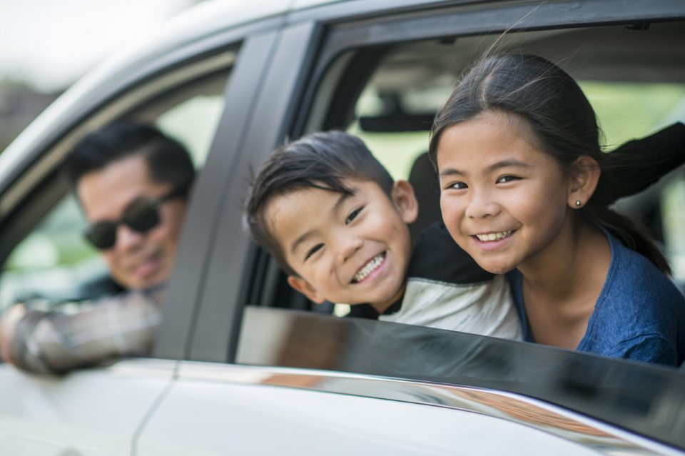 Smiling man and two kids looking out the window of their new Honda