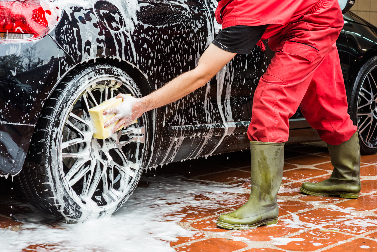 A person cleaning a black midsize sedan. with soap and water. 