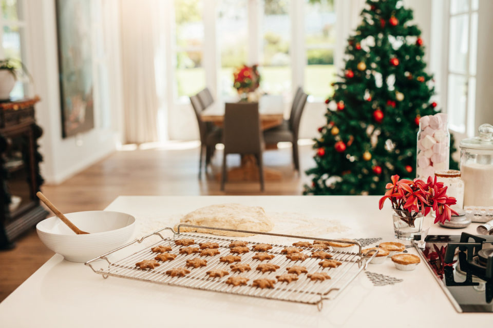 Tray of baked star cookies and dough placed on kitchen table. Decorated Christmas tree in the background.