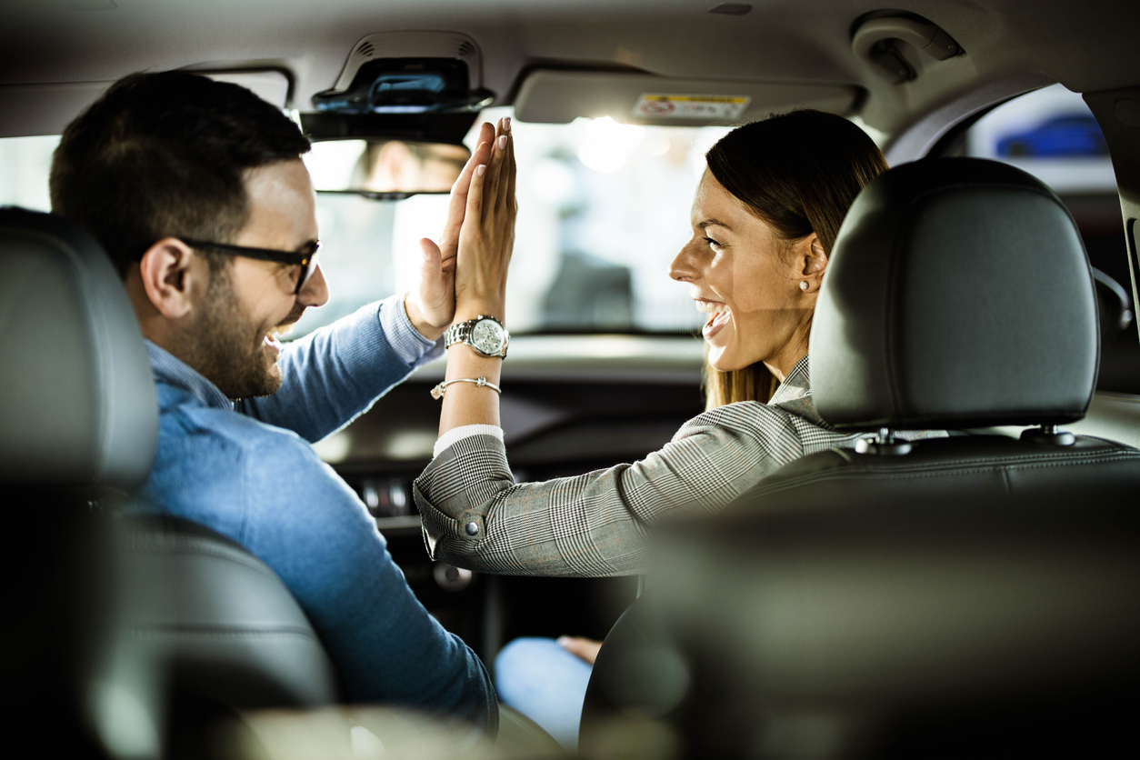 Young happy couple sitting inside of their new car and giving each other high-five