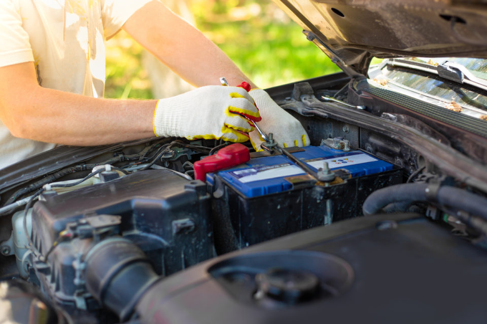 A man unscrews a car battery mount.