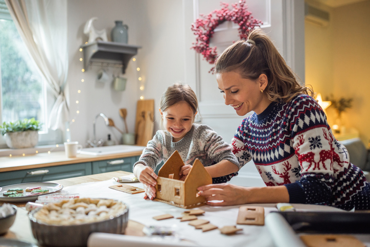 Mother and daughter decorating gingerbread house at home for Christmas.