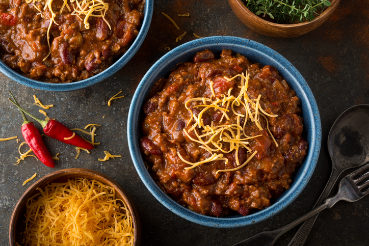 A bowl of delicious home made chili with ground beef, kidney beans, red pepper, tomato and shredded cheddar cheese.