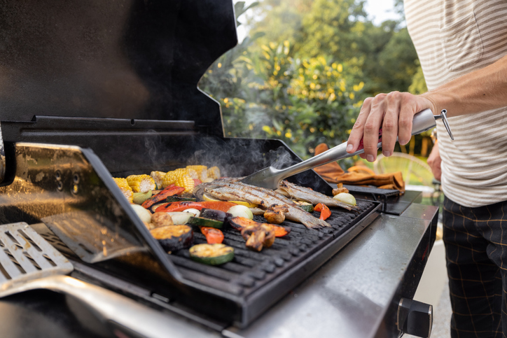 People grilling fish and corn on a modern grill outdoors at sunet, close-up. Cooking food on the open air